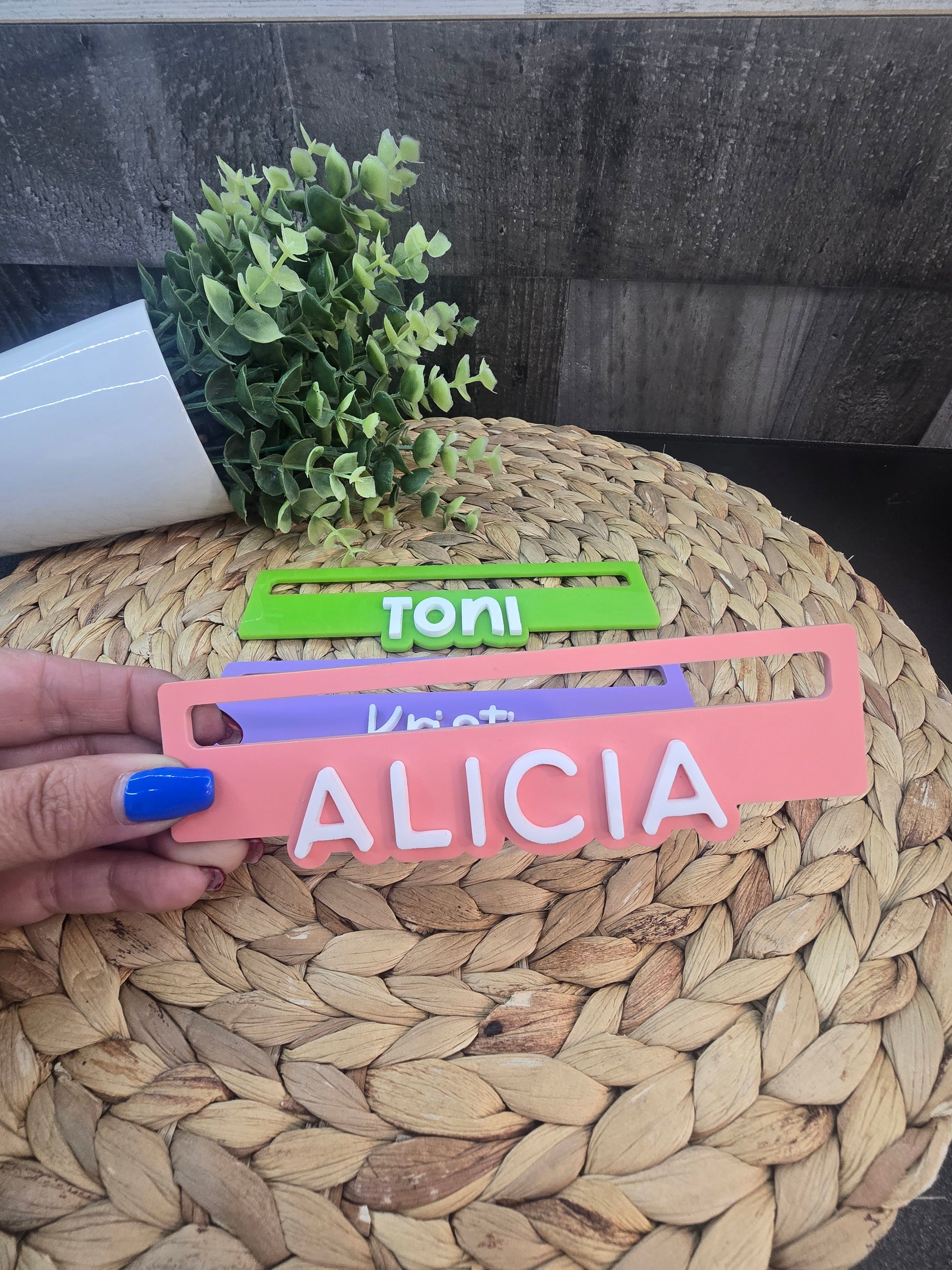 A hand holding a stack of personalized Mahjong line readers engraved with the names Toni, Kristi, and Alicia