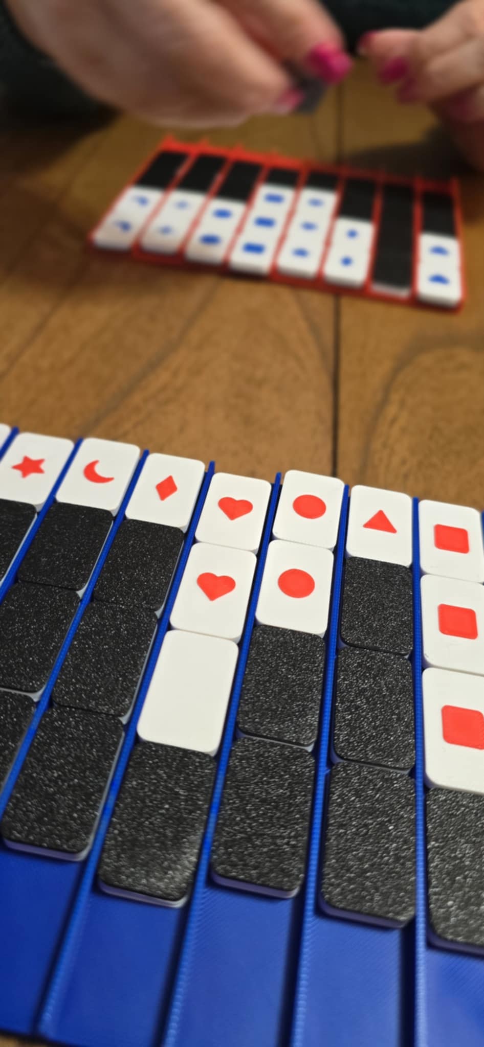 Close-up of a hand arranging red, blue, and black tiles on a wooden surface.